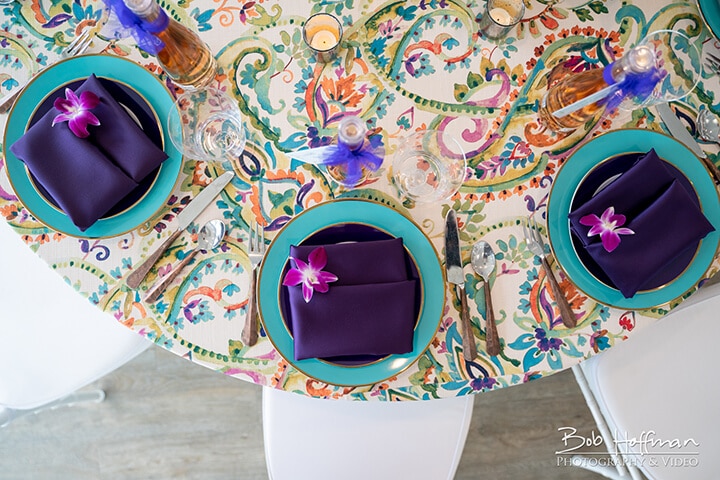 A dining table is set with vibrant, patterned linens, fine china plates, and a floral centerpiece