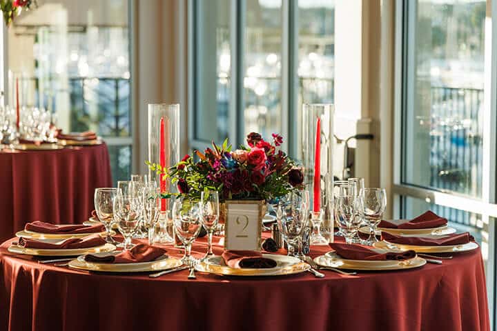 Elegant table setup at our corporate event with pristine glassware, a vibrant floral centerpiece, and sunset-lit windows in the background